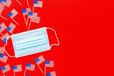 4 Temmuz. Kırmızı arka planda ABD bayrakları ve tıbbi maske. Amerika 'nın Bağımsızlık Günü 2020 Coronavirus covid-19 pandemik karantinası sırasında. Düz konum, üst görünüm, şablon.