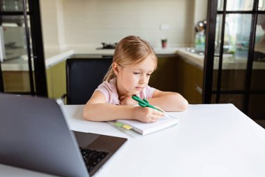 Evdeki online dersi sırasında ödev okuyan güzel bir liseli kız, karantina sırasındaki sosyal mesafe, kendini izole etme, çevrimiçi eğitim konsepti, evde eğitim veren. Oturma odasındaki işyeri