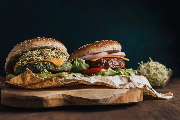 Meat burger and vegan hamburger on top of wooden board with a bowl of sprouted seeds — Stock Photo, Image