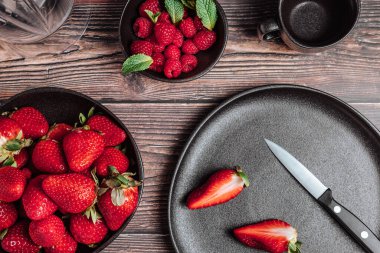 Bir kase çilek, bir kase ahududu, bir fincan çay, dilimlenmiş çilek ve ahşap masada blender ile sakin bir hayat. Boşluk tasarımını kopyala