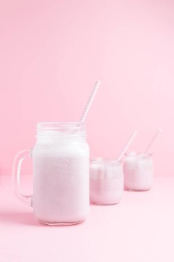 Üç çilekli milkshake seti ve pastel pembe arka planda sürahi. Sağlıklı gıda ve kopyalama alanı tasarımı