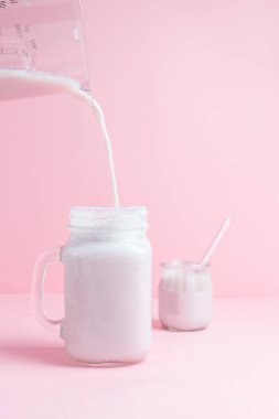 Çilekli milkshake ve sütü pastel pembe arka planlı cam bir kavanoza döküyorum. Sağlıklı gıda ve kopyalama alanı tasarımı