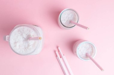 Üç çilekli milkshake 'in üst görüntüsü ve pastel pembe arka planda pipetler. Sağlıklı gıda ve kopyalama alanı tasarımı