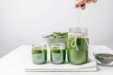 Ispanak kavanozuna iki küçük kavanoz, bir kase chia ve bir kase ıspanak yaprağının yanına Chia döküyorum. Boşluk tasarımını kopyala