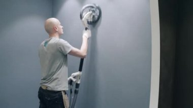 bald man finishes wall repairing using grinding tool