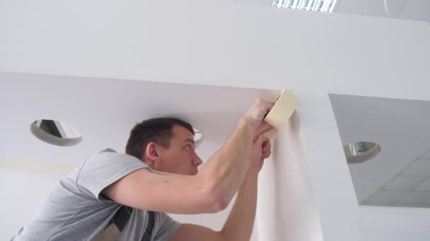 Concentrated handyman in grey jumpsuit glues masking tape — Stock Video