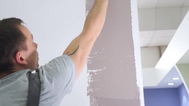 Experienced handyman in jumpsuit colours wall in beige — Stock Video