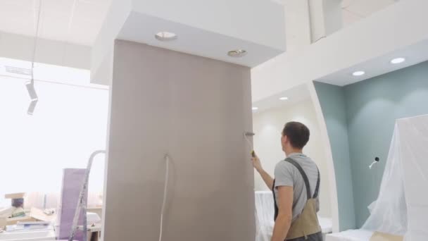 Μυώδης ζωγράφος σε χρώματα jumpsuit μικρός τοίχος σε μπεζ — Αρχείο Βίντεο