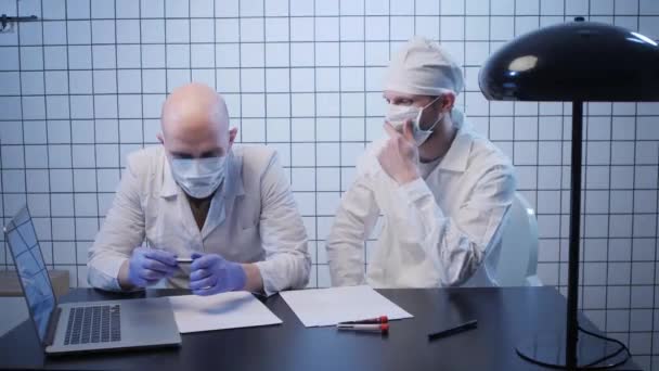 Doctors in coats look at test tube with coronavirus sample — Stock Video