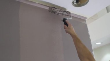 Adam elinde metal paten fırçası ve renkli oda duvarı tutuyor.