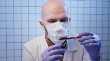 tired bald scientist looks at blood with coronavirus in lab