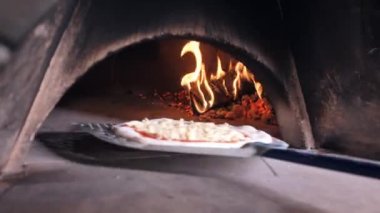 İşçi spatulayı fırına koyar ve pizza hamurunu pişirmesi için bırakır.