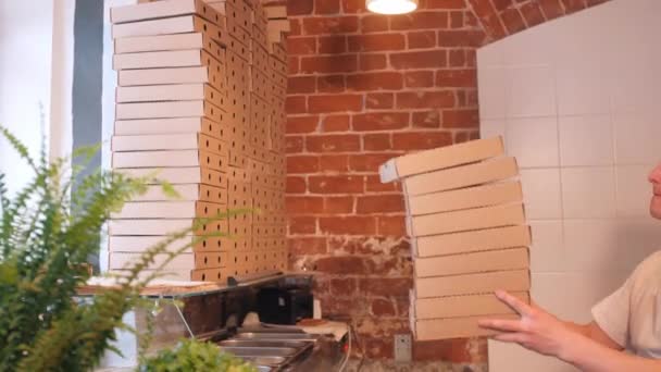Работник пиццерии несет пустые коробки с пиццей и кладет их в стопку — стоковое видео