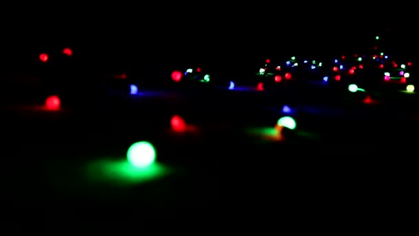 Uma grinalda piscando com luzes brilhantes coloridas deitadas no chão no escuro. Natal e clima de Ano Novo . — Vídeo de Stock