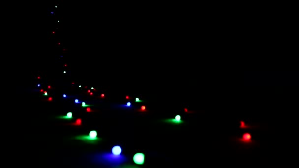 "Flying" over a blinking multi-colored bright lights a garland lying on the floor in the dark. — Stock Video