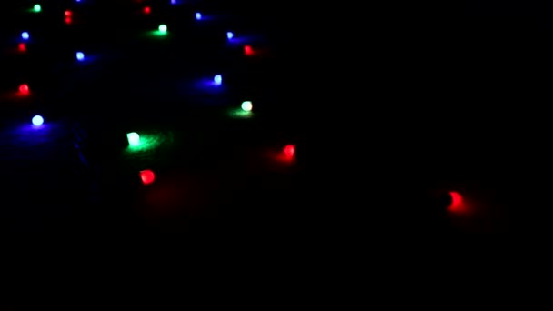 "Flying" over a blinking multi-colored bright lights a garland lying on the floor in the dark. — Stock Video