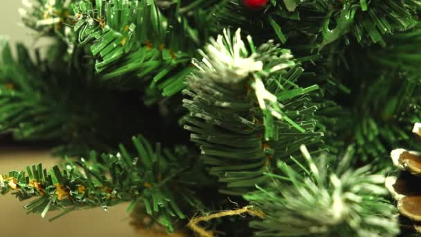 God jul och ett gott nytt år! Grön julgran lätt dammas av snö. Plastträd på en ljus bakgrund med konstgjorda bär och naturliga kottar furu "flyter" framför linsen. — Stockvideo