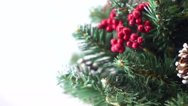 Feliz Navidad y un feliz año nuevo! Árbol de Navidad verde ligeramente espolvoreado con nieve. Árbol de plástico sobre un fondo claro con bayas artificiales y conos de pino natural "flota" delante de la lente . — Vídeo de stock
