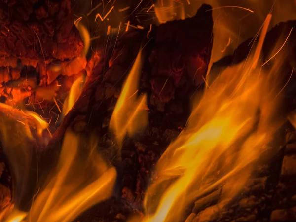 Baile de llamas anaranjadas sobre troncos carbonizados . — Foto de Stock