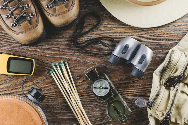 Hiking or travel equipment with boots, compass, binoculars, matches on wooden background. Active lifestyle concept.