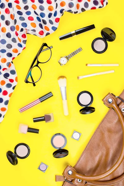 Fashion accessories, makeup products, jewelry and handbag on yellow background. Beauty and fashion concept, flat lay
