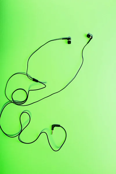 Black in ear headphones on neon green background close up. Minimal music concept. Modern earphones flat lay, top view, modern lifestyle