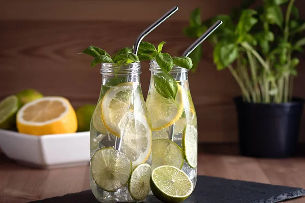 Refreshing drink or water with citrus fruits lemon and lime and basil herb in mason jar with reusable metal straws. Healthy lemonade drink in glass jar, zero waste concept, sustainable lifestyle