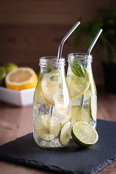 Refreshing drink or water with citrus fruits lemon and lime and basil herb in mason jar with reusable metal straws. Healthy lemonade drink in glass jar, zero waste concept, sustainable lifestyle