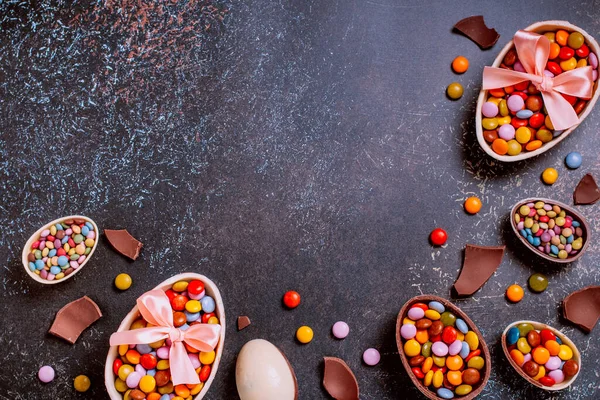 Chocolate Easter eggs and candy on concrete table, festive Easter background flat lay, copy space. Easter card with traditional Easter treats on pink table top.