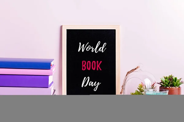 Bookshelf with multicolor books, house plants succulents and black board frame for text. Background for Teacher\'s Day, World Book Day. Still life with stack of colorful books, chalkboard