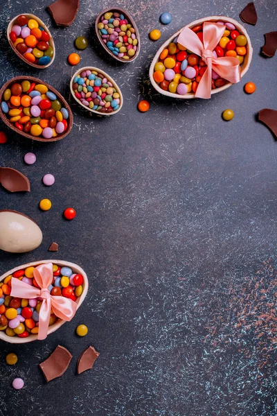 Chocolate Easter eggs and candy on concrete table, festive Easter background flat lay, copy space. Easter card with traditional Easter treats on pink table top.