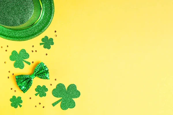 Saint Patricks day holiday card with green shamrock symbols, hat, golden confetti. Traditional St. Patricks Day green attire and decorations on yellow background. Web banner, copy space