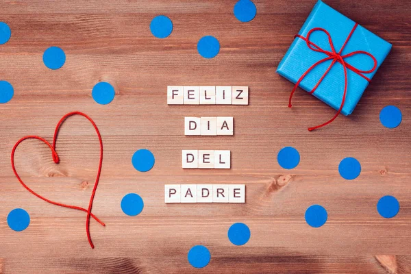 Feliz dia del padre words made of wooden blocks with blue gift boxes and red hearts on wooden background. Happy fathers day greeting card, holiday flat lay