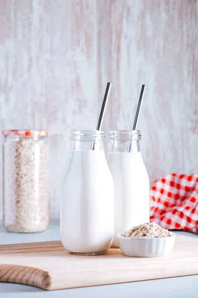 Non dairy oat milk in glass jars with reusable metal straws. Healthy vegan milk alternative still life, copy space. Substitute for traditional cow milk with oat flakes on neutral background