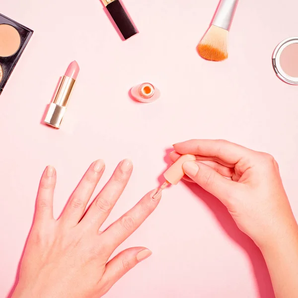 How to get perfect manicure at home concept. Woman doing herself a manicure with makeup items and tools around on pink background. Pastel table top, beauty flat lay
