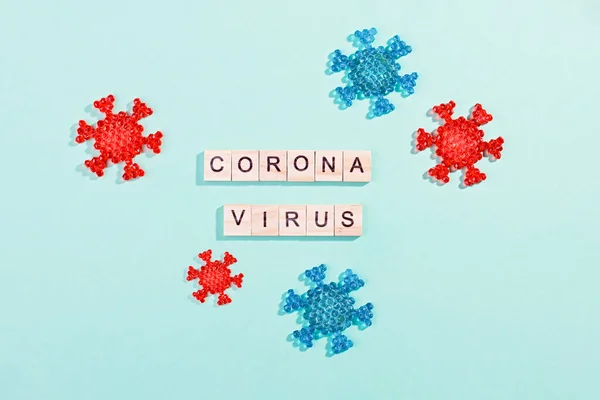 Words corona virus outbreak made of wooden blocks with coronavirus model on blue background, flat lay, top view. Pandemic concept