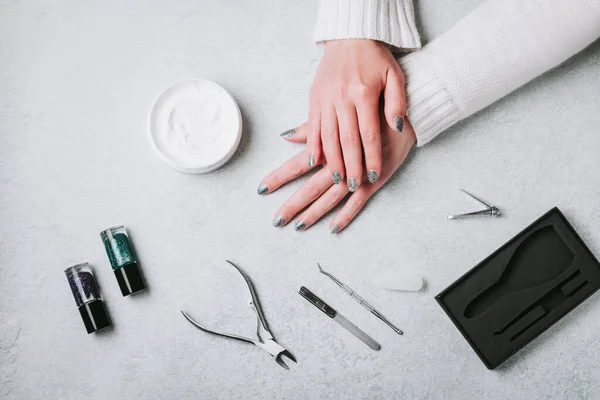 Nail polish, manicure tools and hand cream on grey concrete table top flat lay. How to do manicure at home concept. Do manicure by yourself while staying at home during quarantine, top view