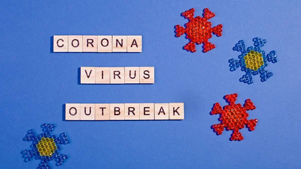 Words corona virus outbreak made of wooden blocks with coronavirus model on light blue background, flat lay, top view. Pandemic concept