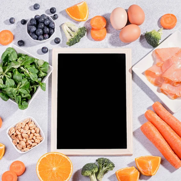 Foods that help maintain eyes healthy, products for keeping good vision. Black board with copy space, assortment of food for eye health on concrete background, flat lay, top view, nobody