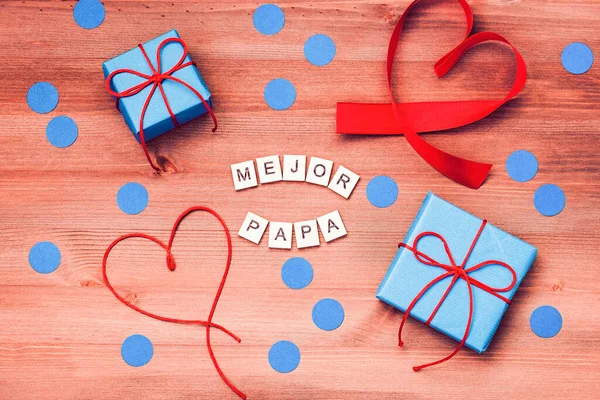 El mejor papa del mundo words that mean best dad in the world made of wooden blocks with blue gift boxes and red hearts on wooden background. Happy fathers day greeting card