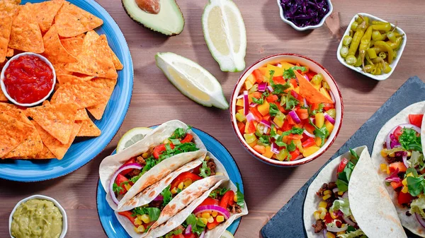 Table with tacos, mango salsa, nachos with sauce, guacamole, lemon beer for Cinco de Mayo celebration party. Appetizers and traditional mexican dishes for family dinner on wooden table top, copy space