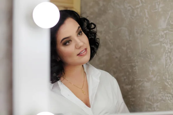 Curly brunette looks in the mirror, the girl admires herself in the mirror, the actress is make-up, the girl is going on a date — Stock Photo, Image