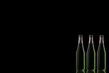 Üç küçük cam şişe ve yeşil içecek sağ arka planda bir ayna yüzeyinde duruyor..