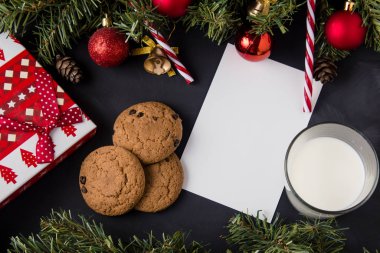 Noel hediyeleri listesi için beyaz çarşaf. Etrafı kozalaklı dallarla çevrili bir masanın üzerinde..