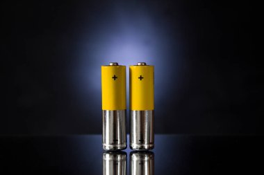 Karanlık bir arka plandaki iki pil bir ayna yüzeyinde duruyor..