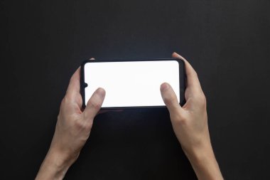 Akıllı telefonu iki eliyle yatay pozisyonda tutar ve başparmakları beyaz ekrana tıklar..