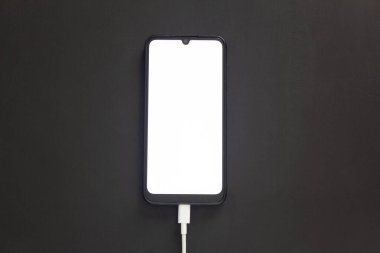 Parlak ekranlı siyah arkaplandaki telefon şarj oluyor..