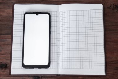 Ekranda ekranı olan telefon, açık bir defterin üzerinde, ahşap bir masadaki kafeste duruyor..