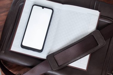 Deri bir çantanın üstündeki açık bir defterde ekranı olan telefon..