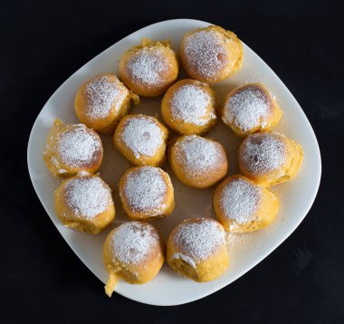 Siyah arka planda beyaz kare bir tabakta bir sürü çörekler var..